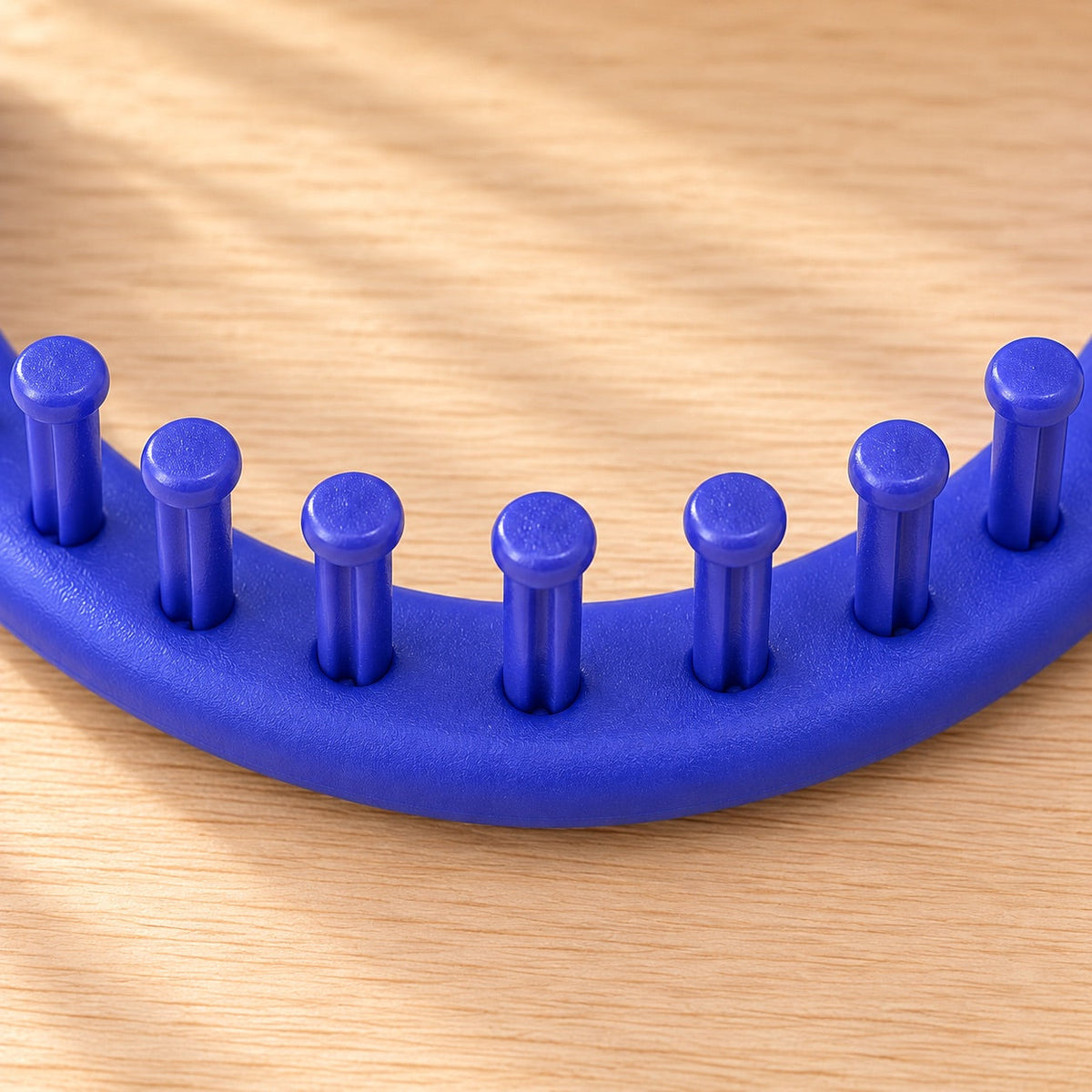AI-styled: Close view of the blue round knitting loom rim and pegs on a warm oak desk. Styling props are not included.