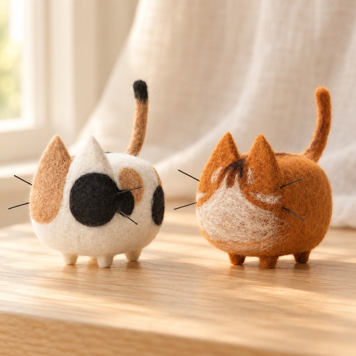 AI-styled: Two finished cat examples from the needle-felting kit on a warm oak desk. Styling props are not included.