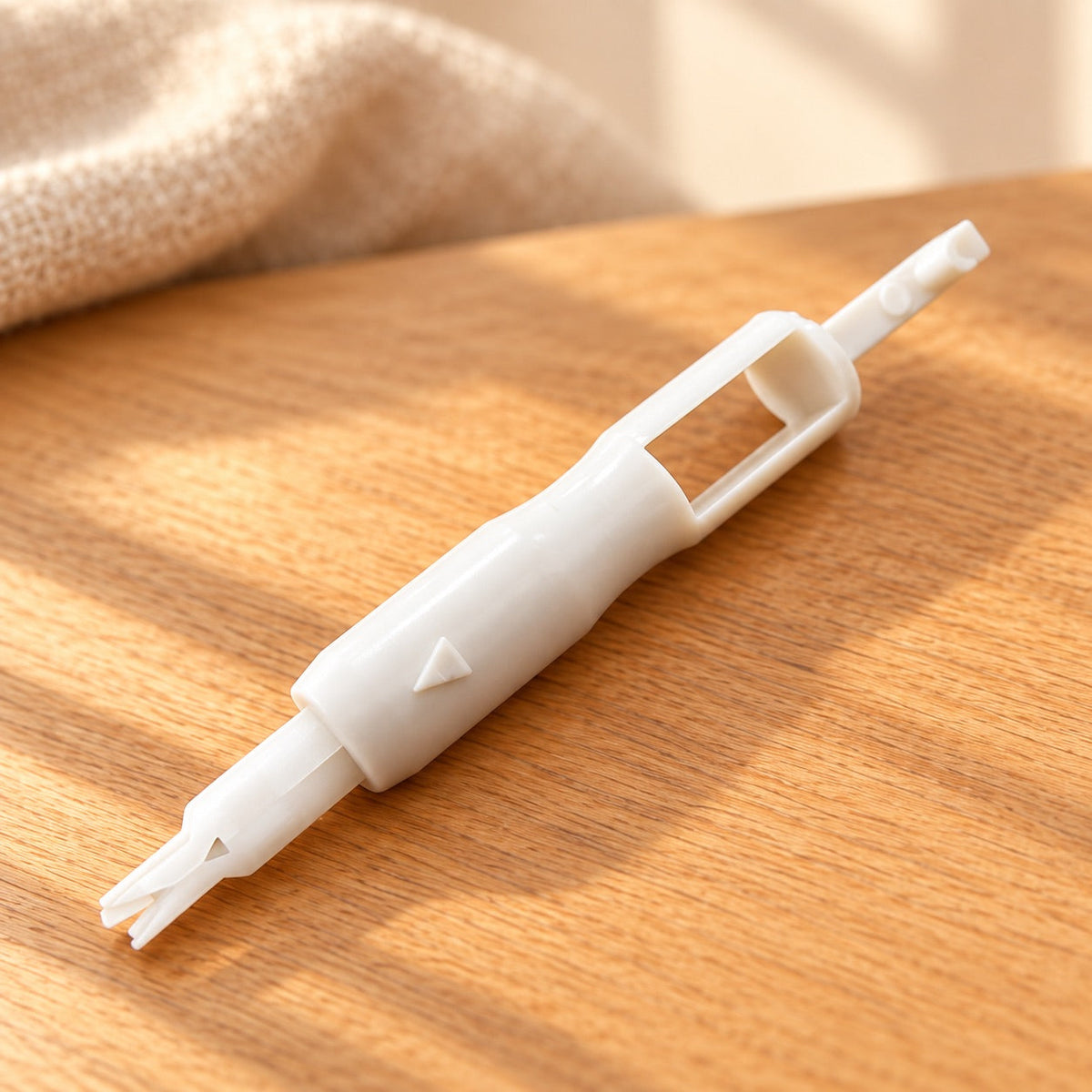 AI-styled: One white sewing machine needle threader from the nine-piece set, closer view on a warm oak worktable. Styling props are not included.
